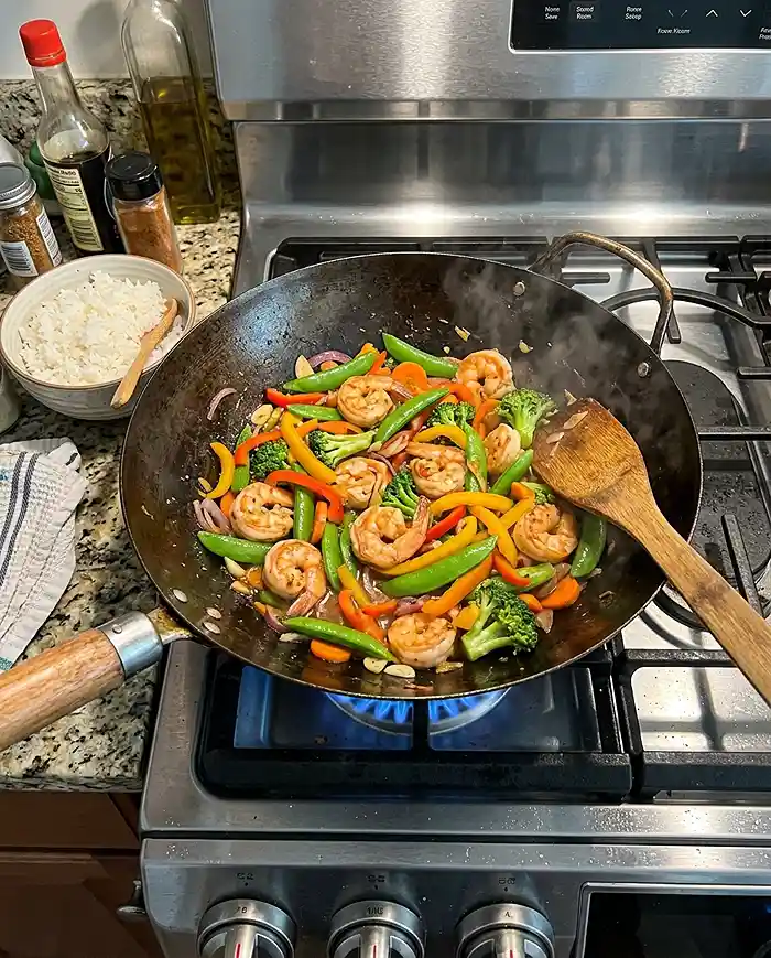 16 Gluten-Free Seafood Recipes 21 Gluten-free shrimp stir fry with colorful vegetables cooking in a wok on a home stovetop
