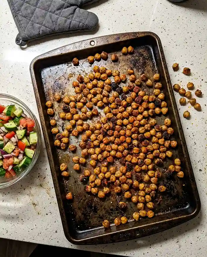 Crispy baked chickpeas on a sheet pan next to a bowl of Mediterranean chickpea salad